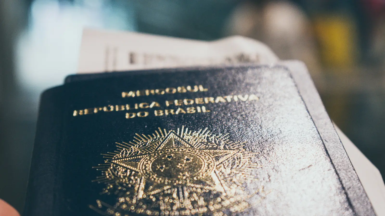 Passaporte brasileiro com um cartão de embarque dentro, segurado na mão num aeroporto
